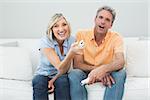 Portrait of a relaxed cheerful couple with remote controls sitting on sofa in a house