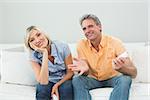 Portrait of a relaxed happy couple with remote controls sitting on sofa in a house