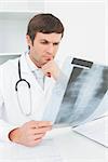 Concentrated male doctor looking at x-ray picture of spine in the medical office