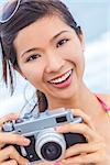 A beautiful Asian Chinese girl or young woman wearing bikini at a beach looking happy taking pictures or photographs with a retro digital camera