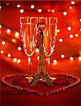 Image of two glass with romantic beverage, little eiffel tower with heart-shaped candles and beads decorated romantic table setting, honeymoon in Paris, festive lights in restaurant, Valentines day