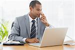 Concentrated young businessman using laptop and phone at the office desk