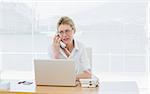 Concentrated young businesswoman using laptop and phone at office desk