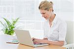 Concentrated young businesswoman using laptop at office desk