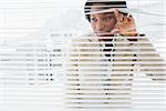 Portrait of a young businesswoman peeking through blinds in office