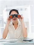 Serious businesswoman looking through binoculars at office desk