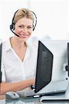 Portrait of a smiling female executive with headset using computer at office desk