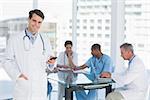 Doctor text messaging with group around table in background at hospital