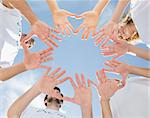 Low angle view of volunteers with hands together against blue sky