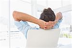 Rear view of a relaxed casual young man resting with hands behind head in a bright office