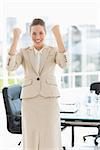 Portrait of a cheerful young businesswoman clenching fists in a bright office