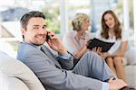 Businessman on call with female colleagues sitting on sofa in background at home