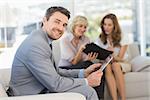 Businessman using digital tablet with female colleagues sitting on sofa in background at home