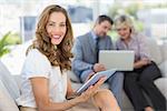 Businesswoman using digital tablet with colleagues using laptop in background at home