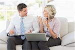 Smart businessman and his secretary with diary and laptop on sofa at home