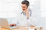 Concentrated male doctor using laptop and phone in the medical office
