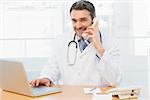 Portrait of a smiling male doctor using laptop and phone in the medical office