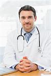 Portrait of a smiling male doctor with laptop sitting at desk in medical office