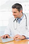Male doctor working on laptop at desk in medical office