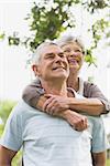 Happy senior woman embracing man from behind at the park