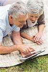 Smiling senior couple using digital tablet while lying at the park