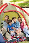 Portrait of couple with kids sitting in the tent at park