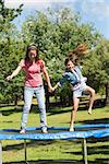 Full length of a happy girl and mother jumping high on trampoline in the park