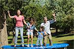Full length of a happy family jumping high on trampoline in the park