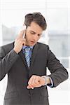 Serious businessman checking the time while on the phone in the office