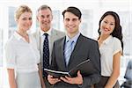 Businessman holding document smiling at camera with his team in the office