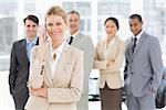 Businesswoman on the phone smiling at camera with team behind her in the office