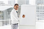 Young happy businessman presenting at whiteboard with marker in the office