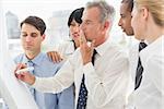 Colleagues watching thinking businessman writing on whiteboard in the office