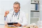 Focused doctor sitting at his desk with clipboard in his office at the hospital