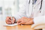 Doctor sitting at his desk writing a prescription in his office at the hospital