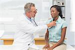 Doctor listening to cheerful patients chest with stethoscope in his office at the hospital