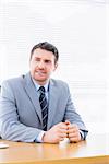 Young thoughtful businessman in suit sitting at office desk