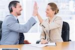 Smartly dressed young man and woman giving high five in a business meeting at office desk