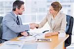 Smartly dressed young man and woman shaking hands in a business meeting at office desk