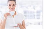 Portrait of a smiling young businesswoman with tea cup standing in a bright office