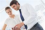 Smartly dressed young man and woman looking at mobile phone in a bright office