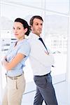 Portrait of a young business couple standing with arms crossed in a bright office