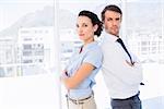 Portrait of a young business couple standing with arms crossed in a bright office