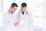 Portrait of two male doctors using digital tablet in a bright medical office