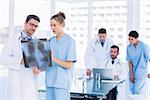 Concentrated doctors examining xray with colleagues using laptop behind in a medical office