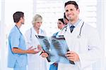 Smiling male doctor examining xray with colleagues standing behind in a medical office