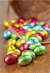 Colorful chocolate Easter eggs on the table and basket in background. Shallow dof