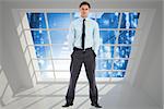 Serious businessman standing with hands in pockets against server hallway seen through window