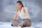 Businesswoman sitting cross legged showing thumb up against urban projection on wall