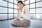 Businesswoman sitting cross legged showing thumb up against room with large windows showing city